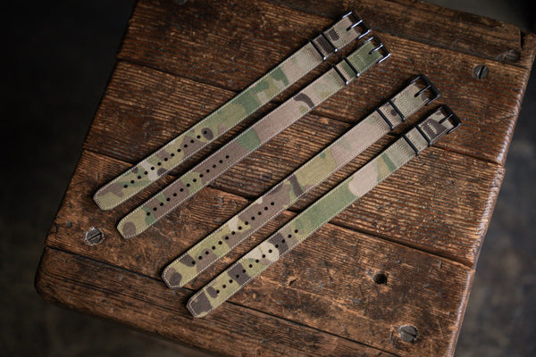 Three camouflage watch straps on a wooden surface